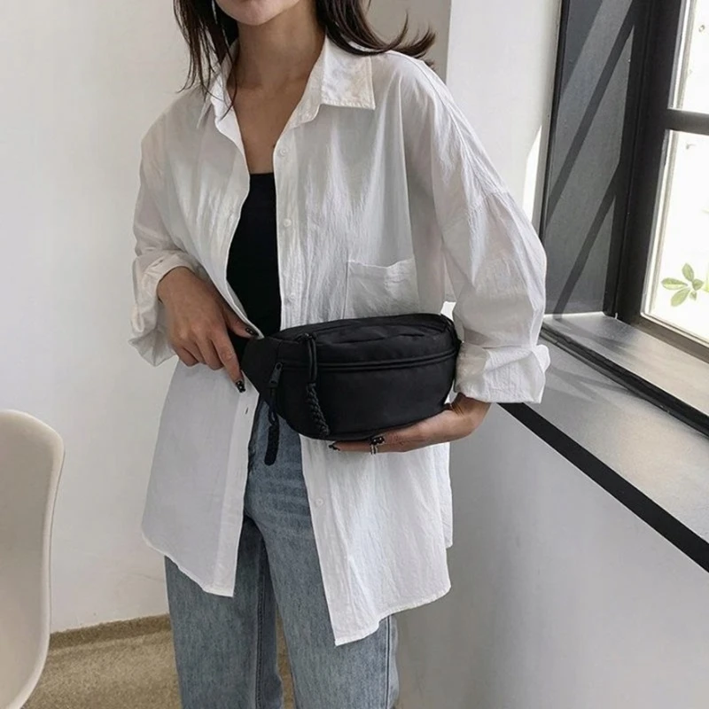 Stylová černá dámská ledvinka TR14 nošená kolem pasu, minimalistický design, praktické kapsy na zip a moderní vzhled pro každodenní nošení.